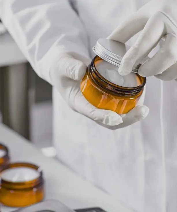 Manos con guantes abriendo un tarro ámbar de crema